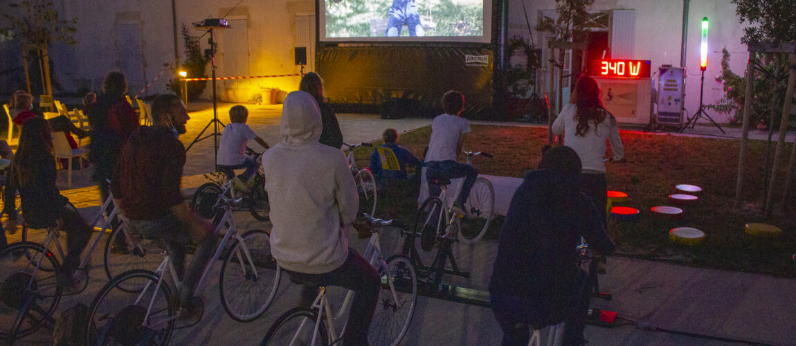 Montage du dispositif Vélo Cinéma de Ludik Énergie, montrant des vélos générateurs connectés à un écran gonflable et à un système de sonorisation en plein air.